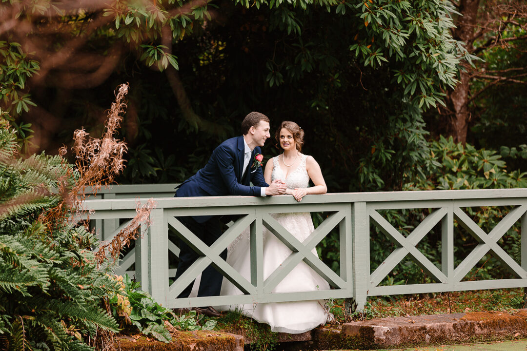 bride and groom leaning on wooden green bridge at larchfield estate wedding